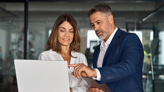 Mature mentor man and European leader woman discussing project on laptop in office. Two diverse partners, colleagues, team of confident professional business people work together. Banner, copy space