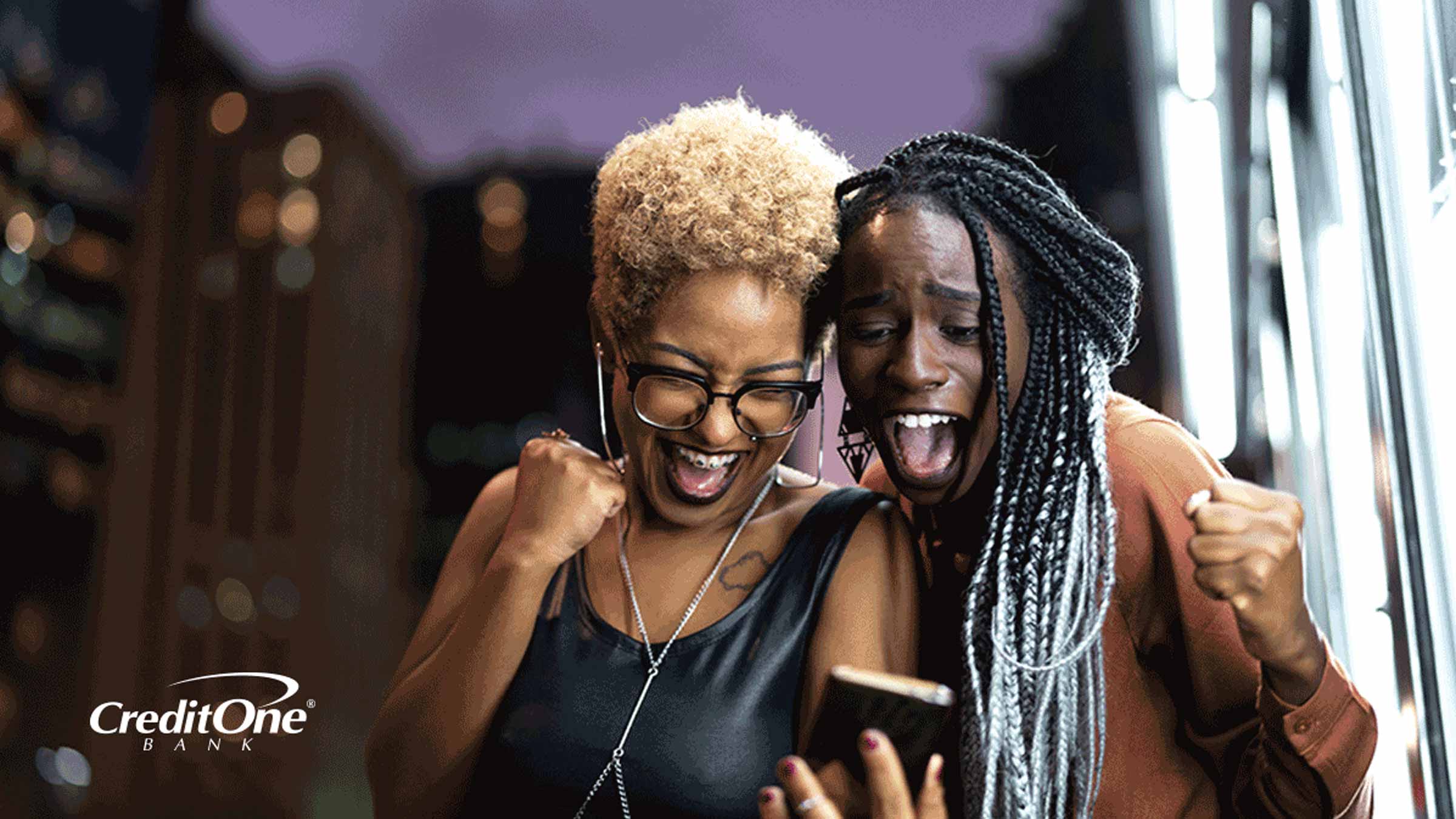 Two women celebrating while looking at a phone